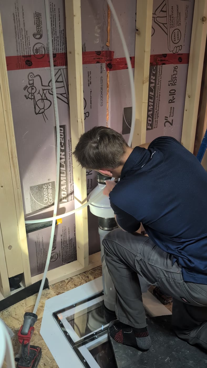 A Radon Solutions Alberta installer working at the suction pit cut through Troy's basement slab, with the new pipe running up the wall.